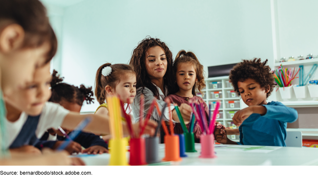 A child care provider and six children coloring at a large table