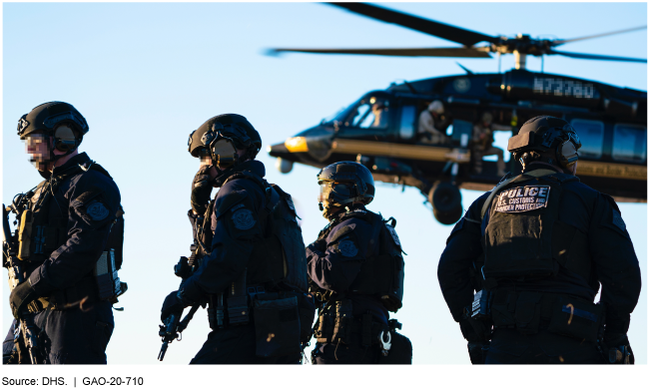 Photo of four special response team members with tactical gear standing outside with a helicopter in the background.