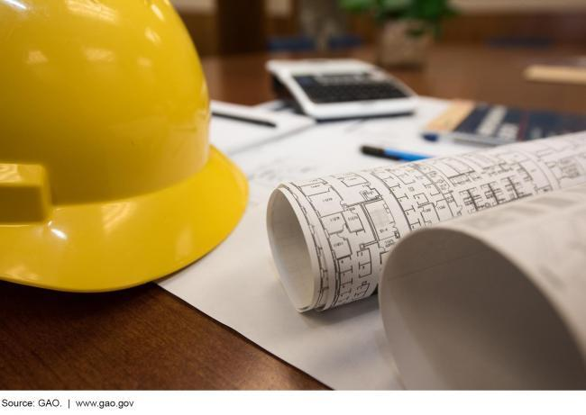 A hardhat, office blueprints, and assorted office supplies on a desk.