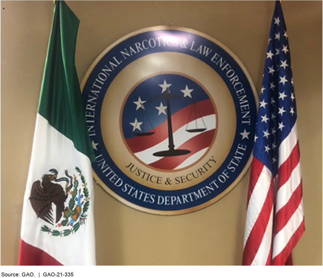 A U.S. Department of State International Narcotics & Law Enforcement seal hanging on a wall with the flags of the United States and Mexico on either side.