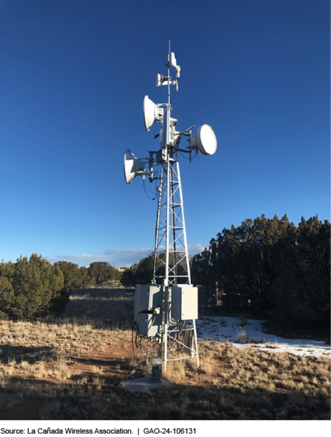 A wireless tower in a rural area, with trees surrounding it. 