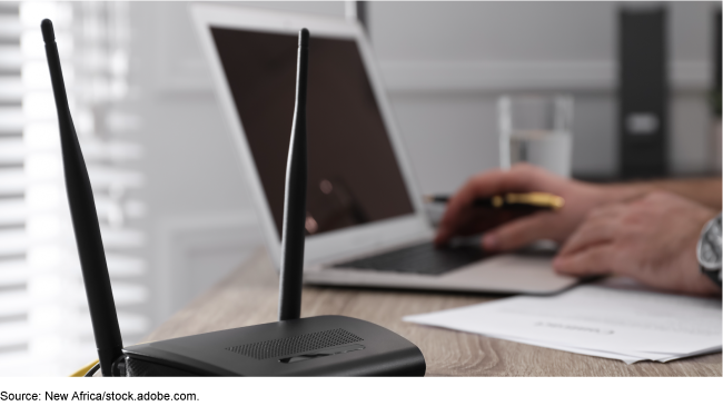 A internet wifi router on a desk next to someone using a laptop.
