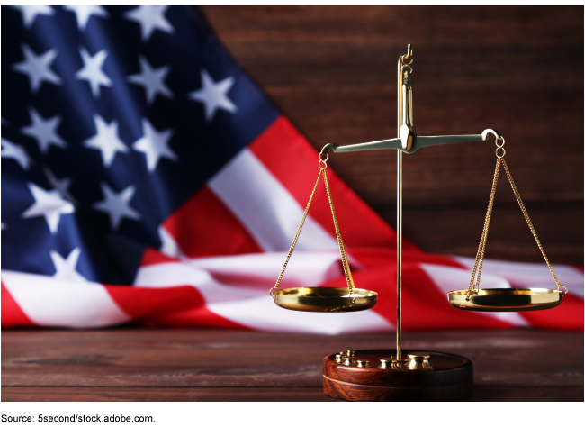 A scale of justice on a table with the U.S. flag in the background. 