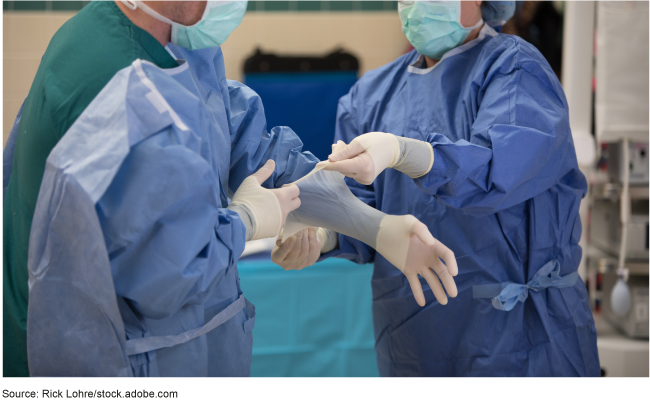 A person wearing scrubs assisting another person wearing scrubs put on gloves.
