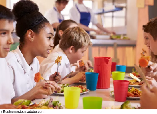 Stock image photo showing students in school uniforms eating lunch together in a cafeteria setting.