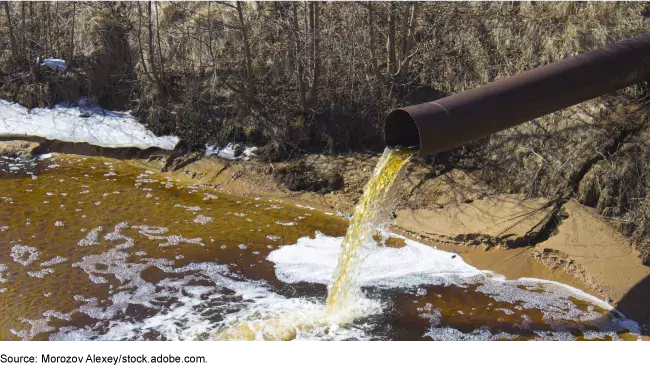 Photo showing water coming out of a pipe with pollution dumping into a stream
