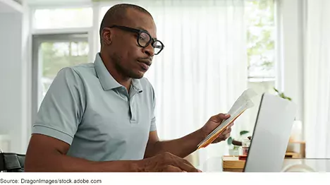 a man looking at paperwork in front of a laptop