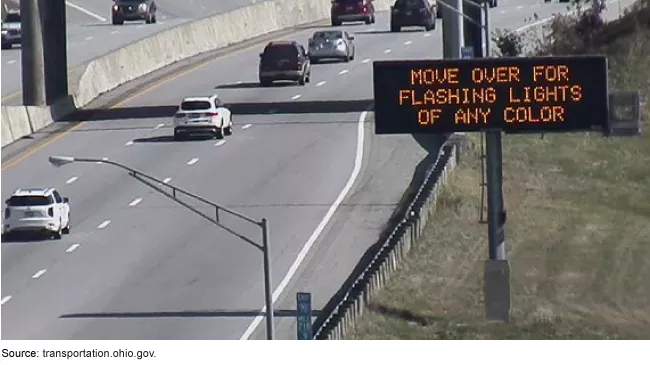 Photo showing an electronic sign on the side of an interstate or highway that reads in orange "MOVE OVER FOR FLASHING LIGHTS OF ANY COLOR."