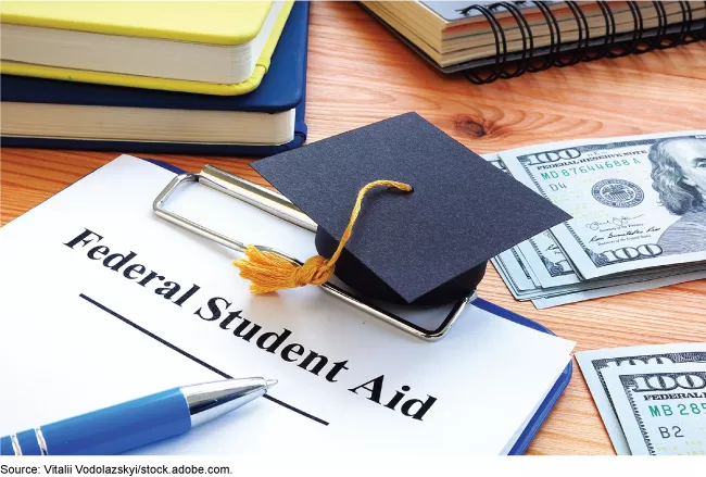 Stock image showing a graduation cap laying on top of a Financial Aid form surrounded by books, notebooks, pens.