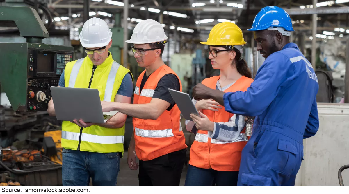 Four people wearing hardhats and reflective vests standing in a factory.