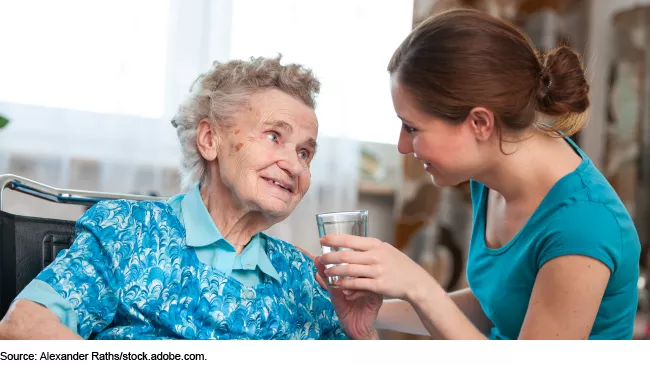 An image showing an elderly woman in a wheelchair being helped by a teenager.