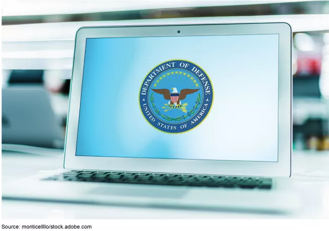 Image showing a laptop on a desk. The screen shows the Department of Defense seal.