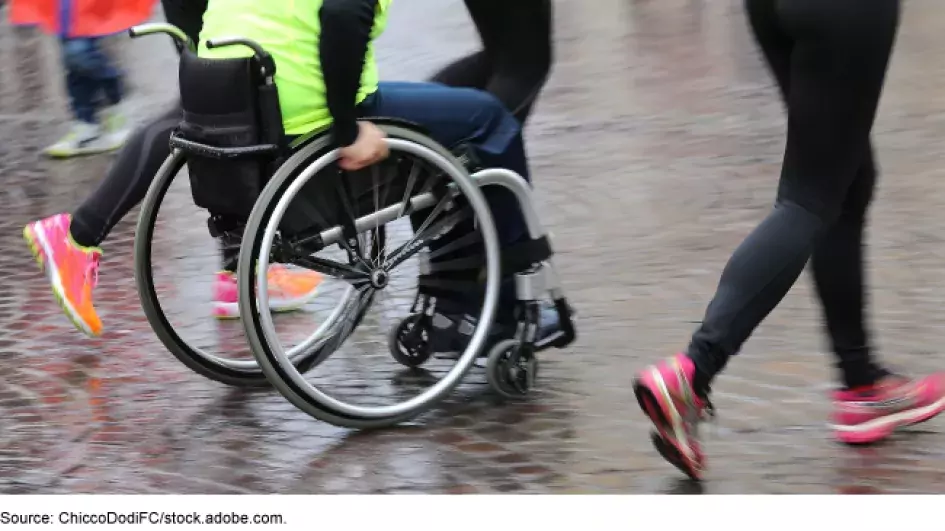 Photo showing a person in a wheel chair next to runners exercising together
