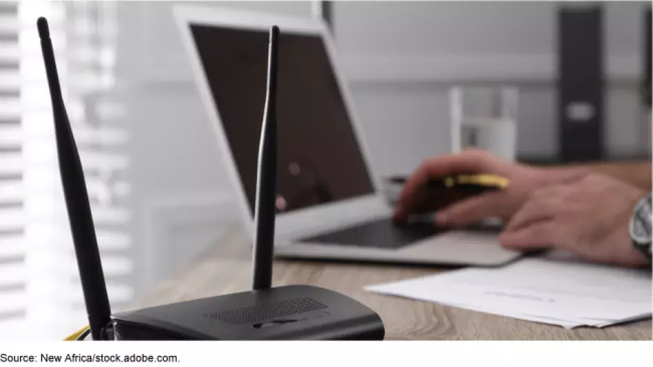 Photo showing a person working at their desk on a laptop with a WIFI router in the foreground 