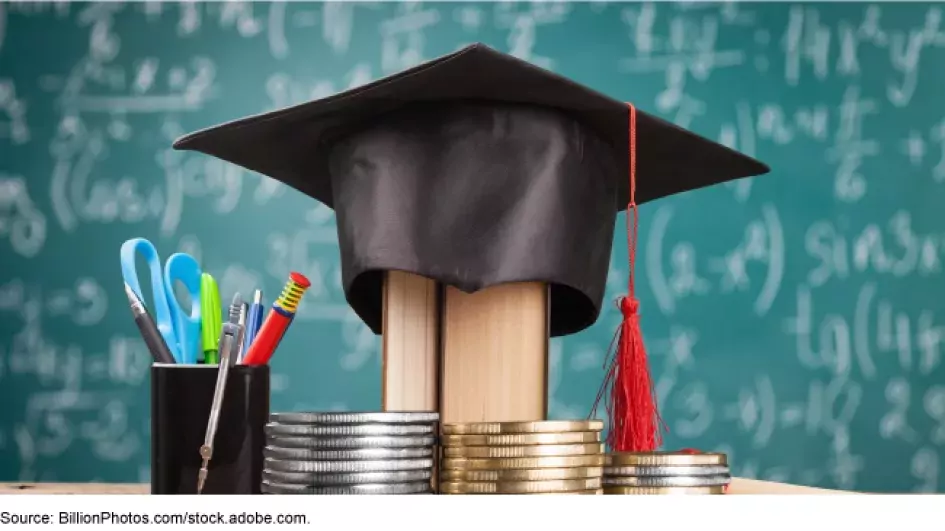 Photo of a grad cap sitting on a pill of coins on a desk, with a blackboard background