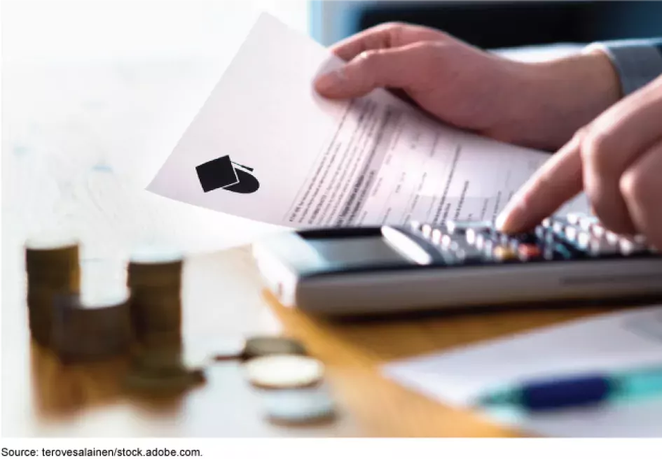 Photo showing a hands on a desk. One hand is holding a financial aid offer (piece of paper). The other hand is on a calculator adding up expenses.