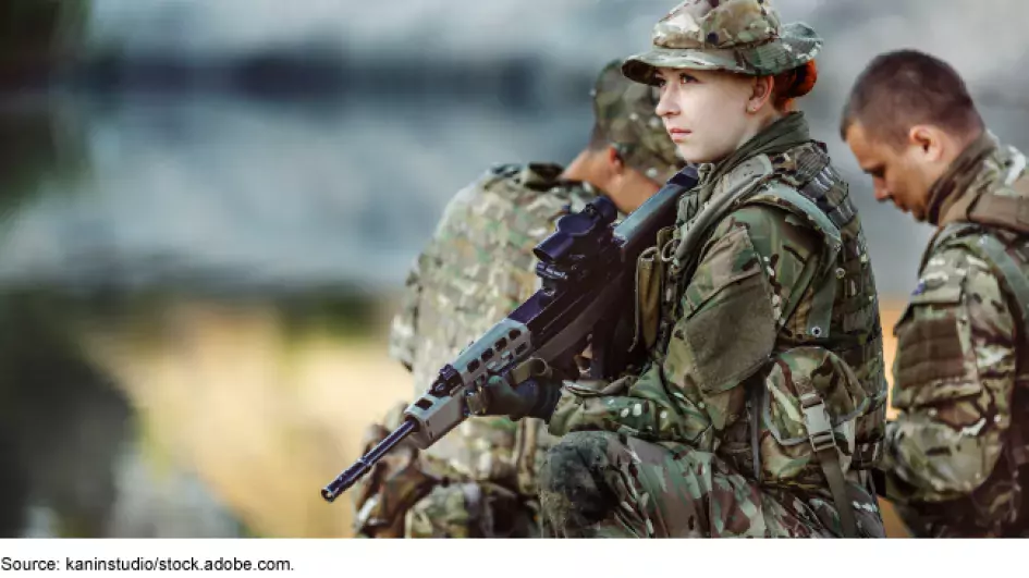 Photo showing a female military servicemember wearing fatigues and caring a military gun.