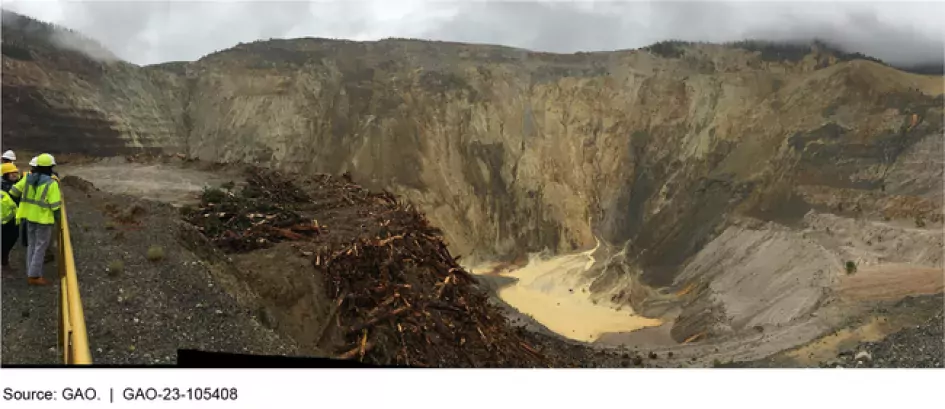 Photograph showing a large pit in the mountains with people wearing construction gear on the side.