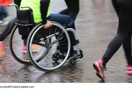 Photo showing a person in a wheel chair next to runners exercising together