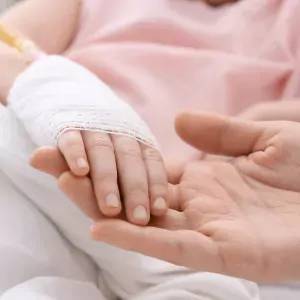Photo showing a child with an IV in her arm holding hands with an adult, maybe a parent or medical worker