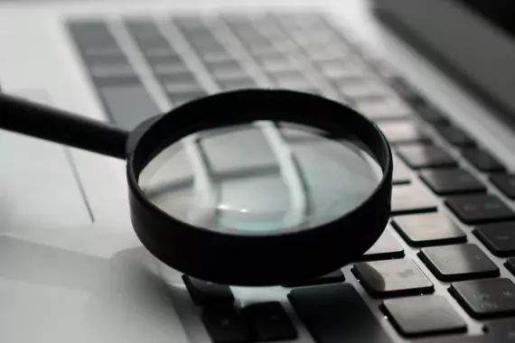 A magnifying glass up against the keyboard of a laptop.